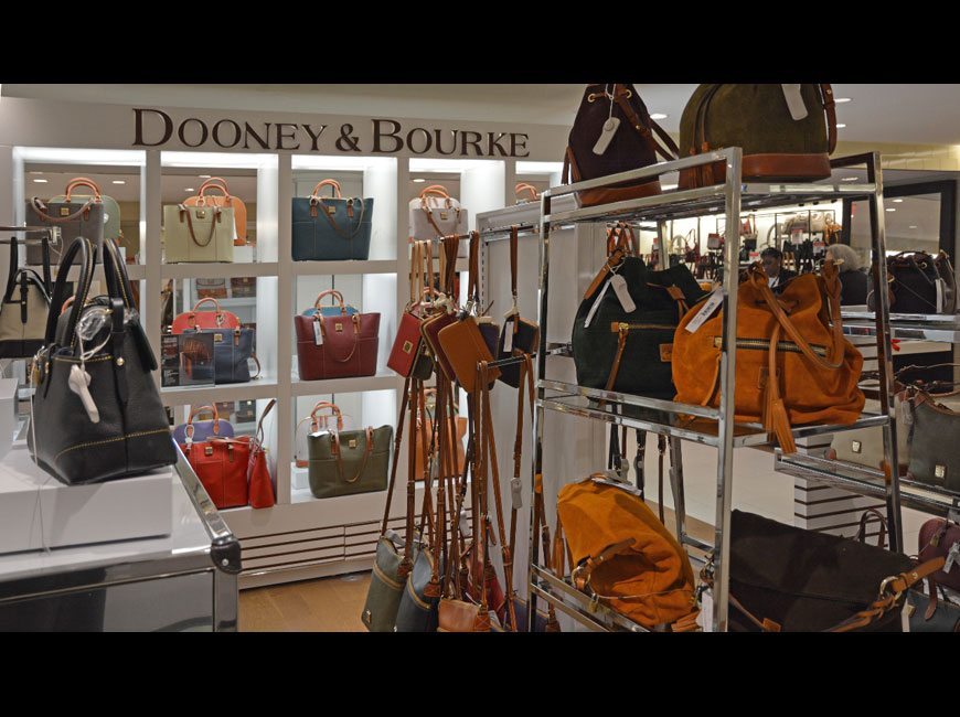 gallery image of custom store-in-store retail interior project featuring custom handbag displays and fixtures, polished stainless steel display shelving, LED lighting throughout, and display pedestals fabricated and installed for dooney & bourke  by Visual Millwork