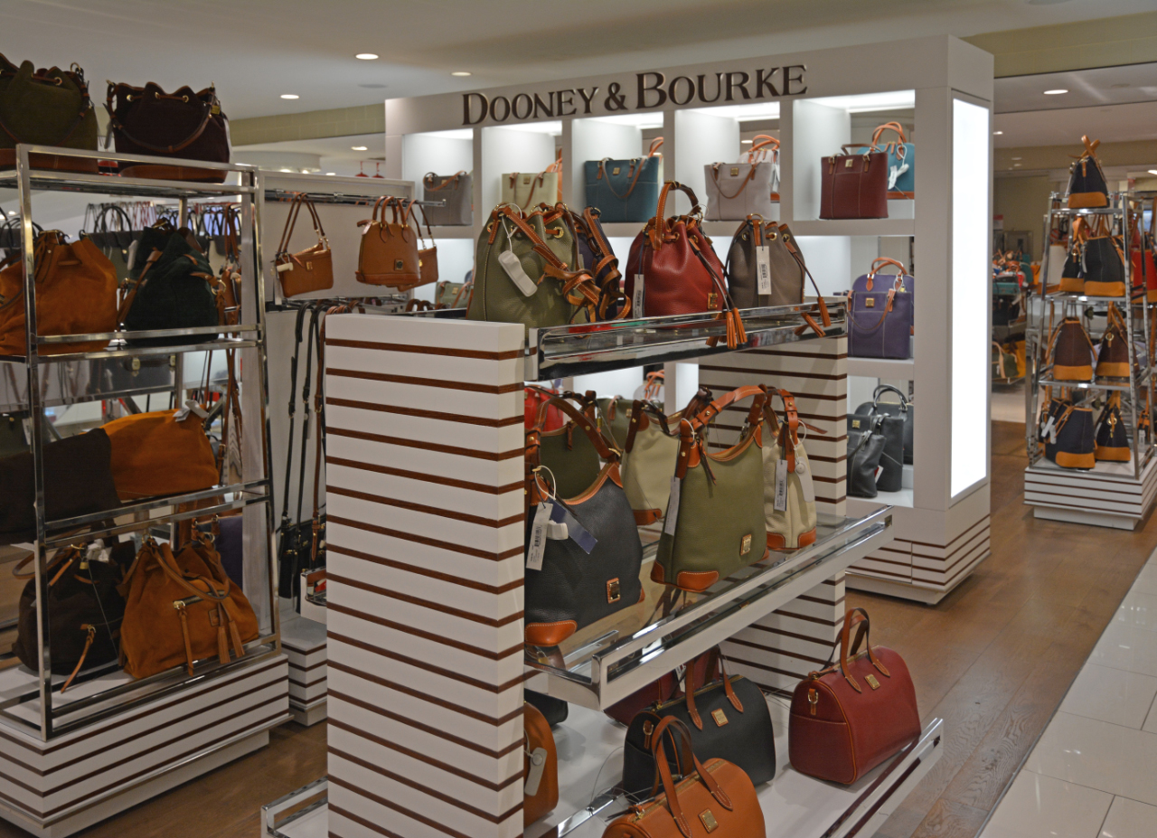 gallery image of custom store-in-store retail interior project featuring custom shelving, custom handbag display, LED lighting throughout, and cable-secured handbag display  fabricated and installed for dooney & bourke by Visual Millwork