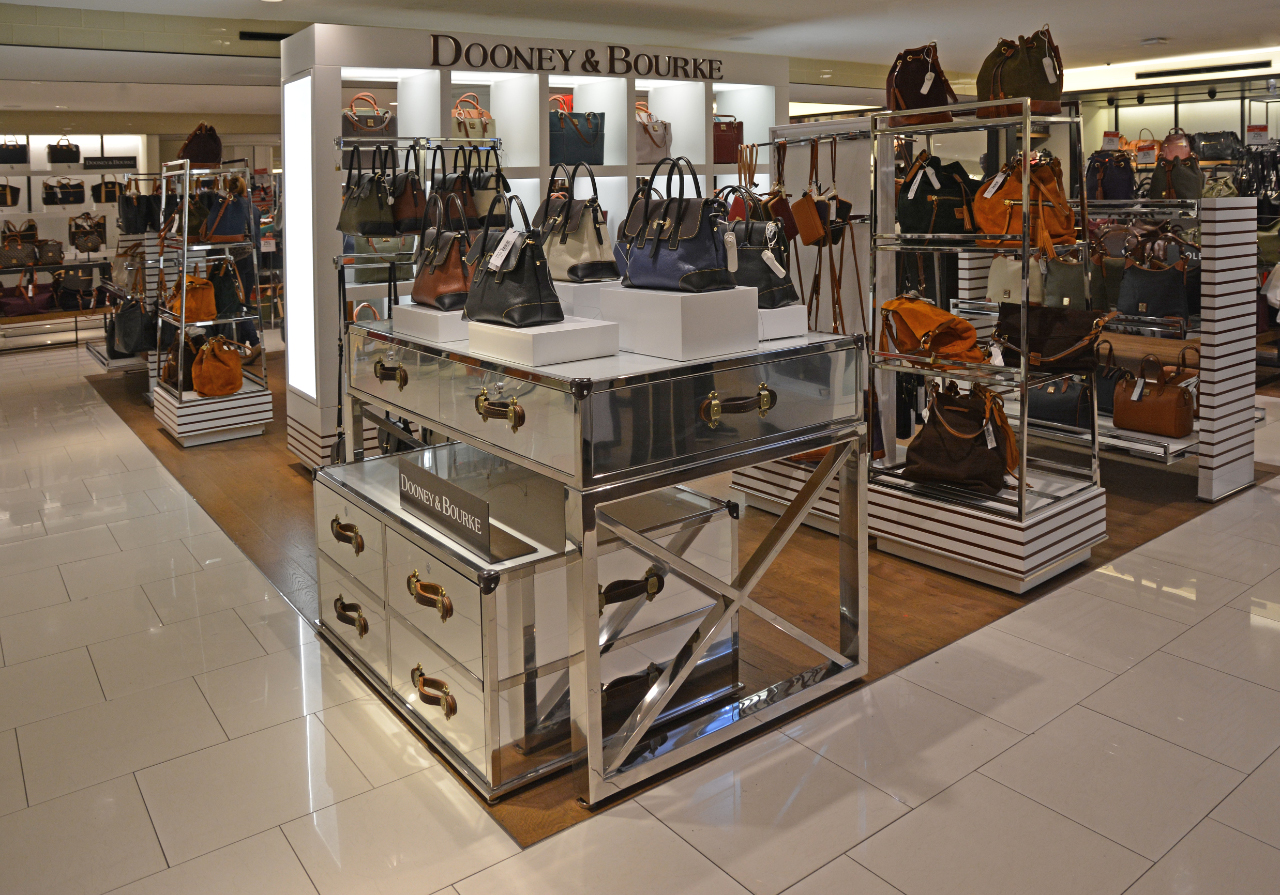 gallery image of custom store-in-store retail interior project featuring custom handbag pedestals, vintage style storage drawers, polished stainless steel display shelving, secure polished stainless steel T-stands, and custom logos and signage fabricated and installed for dooney & bourke by Visual Millwork