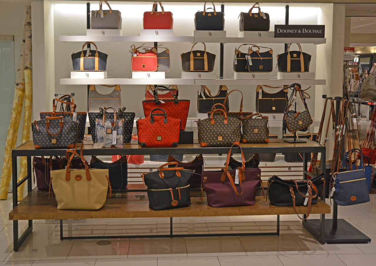 gallery image of custom store-in-store retail interior project featuring custom handbag display shelving, handbag display pedestals, LED lighting, and custom logos and signage fabricated and installed for dooney & bourke by Visual Millwork