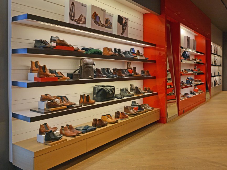 gallery image of custom retail interior project featuring custom perimeter wall, LED illuminated shoe wall, custom shoe display pedestals,and  laminate and wood veneer shoe walls for Dune of London by Visual Millwork