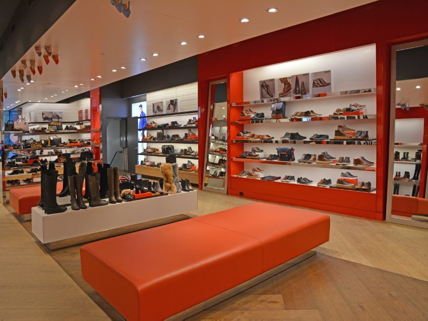 gallery image of custom retail interior project featuring custom seating, custom shoe display pedestals, laminate and wood veneer shoe walls, ceiling suspended shoe display, and LED illuminated shoe walls for Dune of London by Visual Millwork