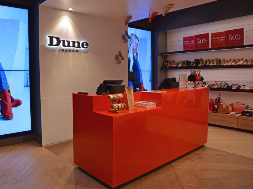 gallery image of custom retail interior project featuring custom cash wrap and custom backlit logo for Dune of London by Visual Millwork
