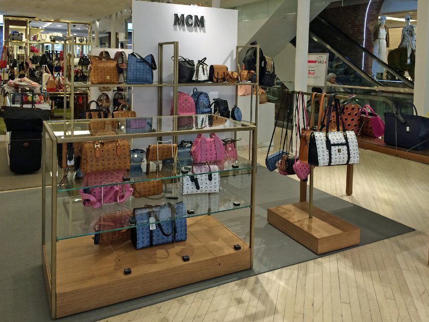 image of  retail interior shop-in-shop custom handbag display project for MCM at Sak's Fifth Ave featuring custom handbag display showcase, custom handbag display rack, and custom handbag display  shelving by Visual Millwork