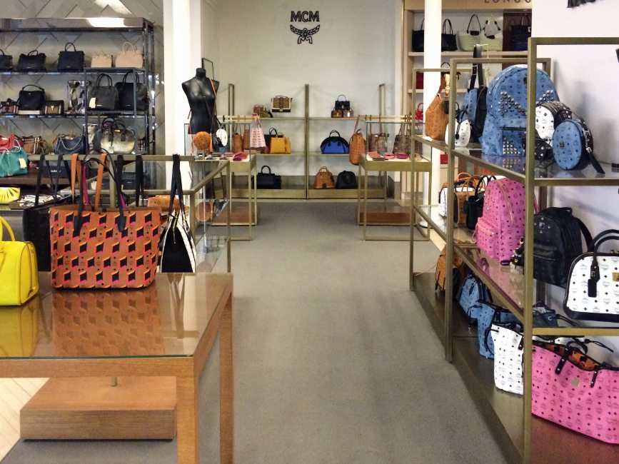 image of custom retail interior shop-in-shop handbag display project for MCM at Sak's Fifth Ave featuring custom handbag display shelving, custom handbag display tables, custom fabricated logo, and secure, custom full view handbag display showcases by Visual Millwork